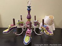 Side view showing multi-coloured shoe-shaped light holders, each detailed with floral and bow decorations, mounted on white metal arms with a central painted piece.