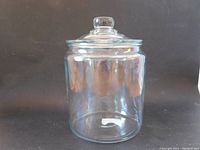 Front view of the clear glass jar with lid on, showing its cylindrical shape and knobbed lid.