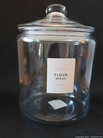 Front view of large clear glass jar with airtight lid and 'Flour Bread' label.