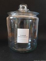 Front view of the large clear glass jar with lid and wheat flour label on black background.