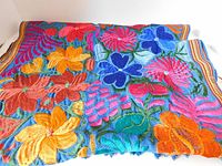 Close-up of vibrant embroidered flowers on handwoven cotton fabric, showing detailed silk embroidery in various bright colors.