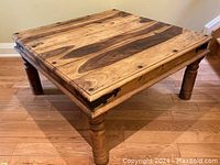 Front angled view of the square solid wood coffee table showing the wood grain top, sturdy turned legs, and metal corner accents.