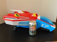 Large red, blue, and white jet next to a soda can for scale