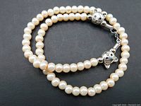 Blush cream simulated pearl necklace coiled to show silver plated engraved kitty clasp in close-up.