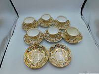 Top down view of 6 cups and 8 saucers with visible gilding and floral patterns