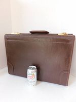 Front view of large vintage brown leather litigation case, showing smooth leather surface, handle on top, and gold-tone flip locks. Positioned next to a soda can for size reference.