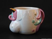 Front side view of the unicorn mug showing the handle, gilded horn, stars, and swirl mane in pastel colors under metallic glaze.