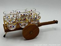 Six glass shot glasses with colorful polka dots arranged in a wooden cart with wheels, showing the overall set and details of the glassware and cart.