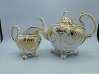 Teapot and creamer side by side showing full ornate Baroque style and hand-painted details.