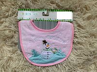 Photo of pink baby bib showing front with embroidered snowman and holiday themed decoration along with 'Mon Premier Noël' text.