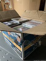 Open cardboard box filled with stacked music CDs in jewel cases, some album covers visible.