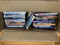 Top view of cardboard box filled with DVDs showing spines and some covers from multiple genres and decades