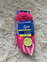Photo of two pairs of bright pink Dr. Scholl's Spa socks bundled together on a light shag carpet background. The socks are thick and soft with white trim and are labeled new, size 4-10 with grippers on the soles.