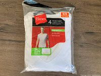 Photo of a Hanes package containing 4 white tagless V-neck T-shirts, size Medium. Package is partially opened, showing 2 shirts remaining.