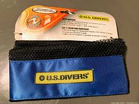 Photo showing the blue and black mesh gear bag with U.S. Divers logo patch and packaging branding, indicating it is a mesh gear bag designed for adult snorkelling and water sports use.