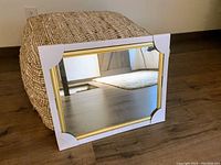 Photo shows two rectangular mirrors placed on floor leaning against a pouf and wall; protective corner covers on the frames visible