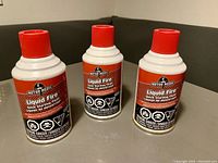 Photo of three Motor Medic Liquid Fire Quick Starting Fluid cans with red caps arranged upright on a surface.