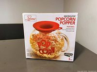 Box front showing Laroma Micro-Pop Popcorn Popper in clear glass with red silicone lid, labeled features and 3 quart capacity