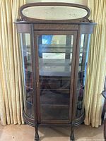 Front view of antique oak curio cabinet showing curved glass sides and straight-cut front glass door with cracked glass panel.