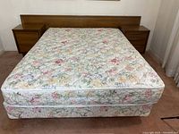 Front view of floral patterned mattress and boxspring on metal bedframe with wooden headboard and nightstands in background