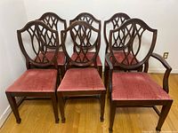 View of five vintage dining chairs and one captain chair all with wooden carved backs and pink upholstered seats arranged in a group.