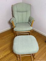 Front view of the Dutailier light green glider chair with matching ottoman in a corner on wood floor.