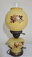 Full lamp front view showing yellow glass globe with floral painting and clear chimney.