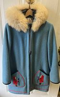 Front of blue wool coat with fur trimmed hood and embroidered pockets featuring a person in red parka figure.
