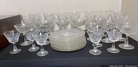 Crystal glassware set shown front and center on black fabric surface including side plates and assorted stemware.