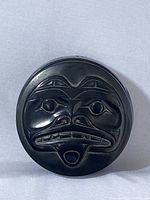 Top view of round trinket box lid showing detailed carved Native Alaskan style face with eyes, nose, mouth and tongue.