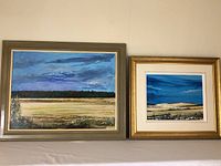 Both framed paintings shown side by side on a table surface, blue sky and field landscapes visible.
