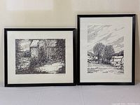 Two framed ink sketches by R.J. Robertson displayed side by side on a white surface against a beige wall. Both depict rural scenes.