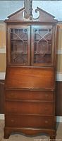 Front view of entire vintage secretary desk with bookcase showing glass doors, drawers, and slant-top writing surface.