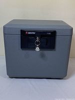 Front view of the gray Sentry Safe 1180 closed with key in lock.