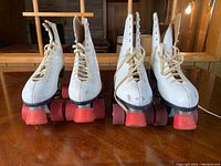 Front view showing a pair of white high-top leather roller skates with red wheels on a wooden surface.