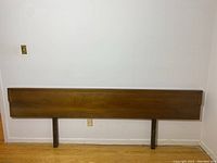 Full view of walnut headboard mounted on wall, showing two support legs