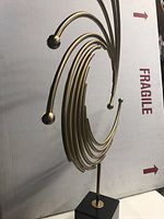 Side angle view showing curved metal rods in circular wave design mounted on black granite base.