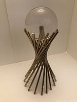 Crystal ball mounted on modern twisted metal stand sculpture under bright lighting.