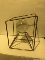 Metal geometric frame sculpture with suspended 3-inch clear crystal ball, shown from angled front view.