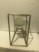 Front and side views showing the gold-tone geometric metal frame and suspended clear crystal ball inside.