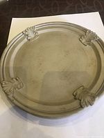 Top view showing the circular plate with four stylized leaf/feather decorative motifs near the rim.