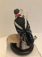 Figurine of a Great Spotted Woodpecker perched on a birch log with mushrooms, viewed from behind showing detailed feather and red markings.