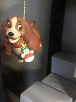 Photo of vintage Lady and the Tramp Christmas ornament showing detailed front view of Lady holding a snowman figurine on a gold hanging string.