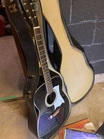 Black Raven acoustic guitar standing inside a hard shell case, showing overall condition and guitar body details.