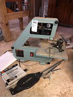 Front view of King 10" band saw with attached power switch and additional woodworking blades in a Black & Decker box, showing floor placement and surrounding environment.