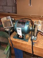 Full view of Manchu bench grinder on wooden workbench, showing motor housing, label, tool rests, and power cord.