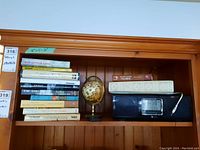 Photo showing shelf with stack of books, small desk globe and a Teac model RC-1079 radio with clock display and remote control