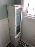 Tall white MDF cabinet placed in corner next to window, showing full height and overall shape.