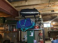 Photo of camping bags stacked on metal shelving with two red base lanterns and a green Coleman metal lantern case below them
