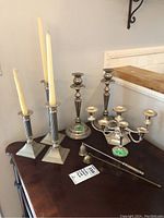 Full view of all candle holders and accessories on wooden table showing set of seven candle holders and snuffer.